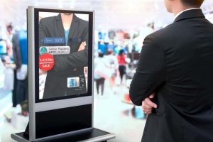 Man stands in front of digital signage, looking at a picture of another man in a suit with his arms crossed.