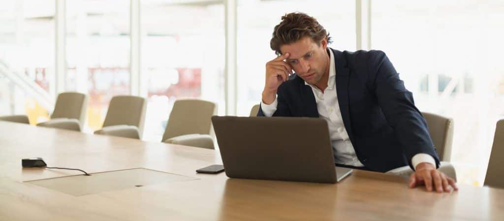 Worried businessman sits at computer in office, worrying about how to improve his SMB security.