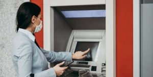 A young lady accesses an ATM while taking precautions due to Coronavirus.