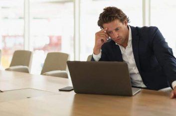 Worried businessman sits at computer in office, worrying about how to improve his SMB security.